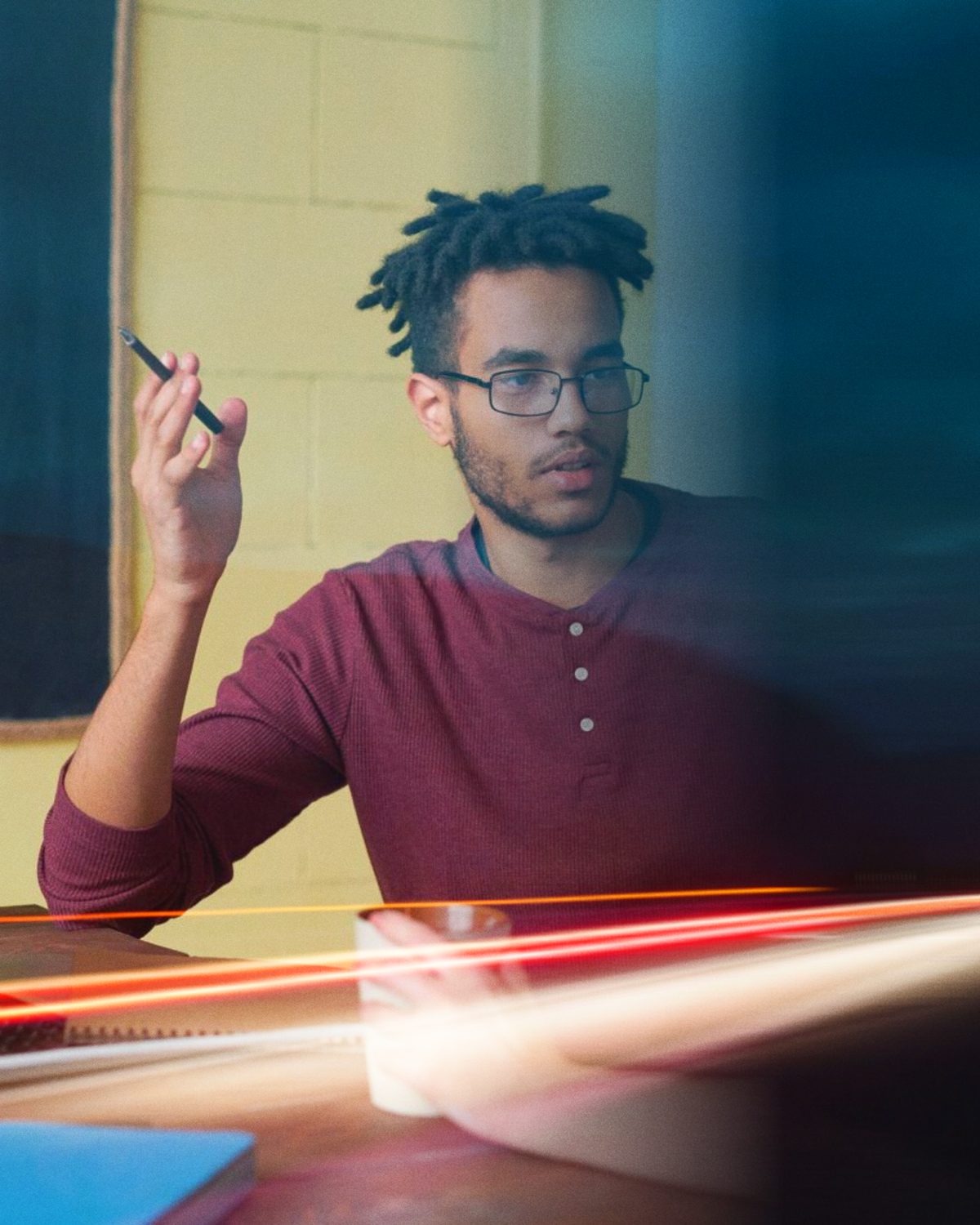 A man in glasses making a point in a meeting, pen in hand, with streaks of light passing in front